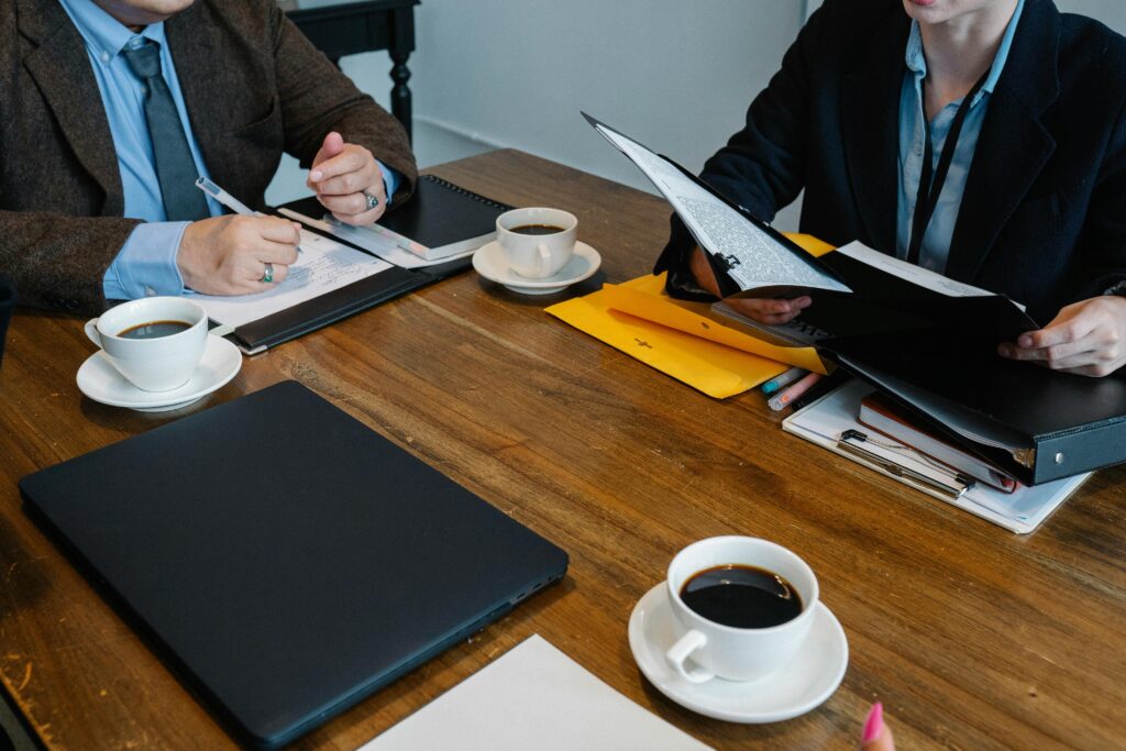 Crop unrecognizable coworkers in formal clothes sitting at table with documents and cups of coffee from friends coffee bar while working together